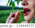 A woman holding a single red cherry between her teeth 118449575