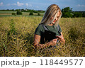 A woman farmer checking the quality of rapeseed in the field, holding a tablet and rapeseed in her hands 118449577