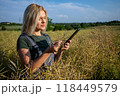 A woman farmer standing in the middle of rapeseed field and checking the information about a harvest on a tablet 118449579