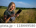 A woman farmer checking the quality of rapeseed on the field, holding a tablet and smiling 118449580