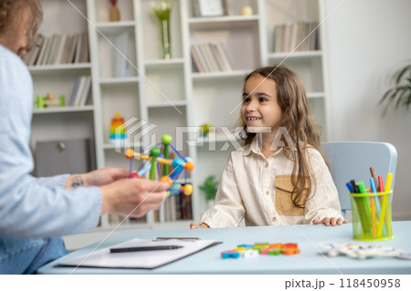 Cute long-haired girl looking busy while having a tutorial with a speech therapist Cute long-haired girl looking busy while having a tutorial with a speech therapist 118450958