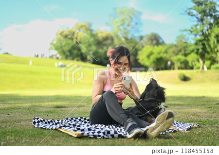 Cheerful young woman resting on a blanket with her dog after workout and using mobile phone Cheerful young woman resting on a blanket with her dog after workout and using mobile phone 118455158