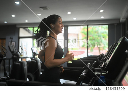 Side view of sporty woman running on a treadmill at gym and listening music 118455209