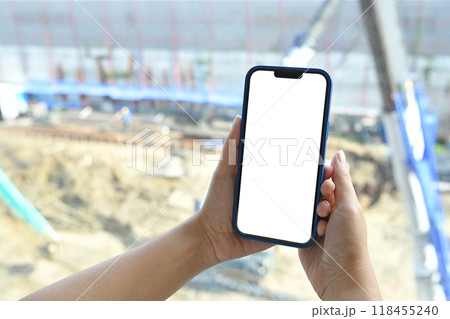 Close up of hands holding smartphone with blank screen on construction site in the background Close up of hands holding smartphone with blank screen on construction site in the background 118455240