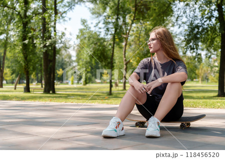 Easygoing portrait highlighting a young female's confident poise as she sits atop a skateboard, representing the independent, athletic nature of modern youth culture Easygoing portrait highlighting a young female's confident poise as she sits atop a skateboard, representing the independent, athletic nature of modern youth culture 118456520