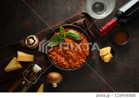 Bolognese sauce in frying pan, ingredients, glasses and bottle of wine on dark background, top view 118456880