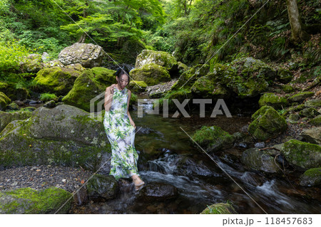 渓流の苔むした岩に座り水に足をつける女性 118457683