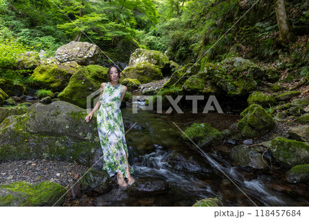 渓流の苔むした岩に座り水に足をつける女性 118457684