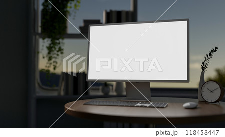 A close-up of a computer with a white screen mockup on a hardwood round table in a dark room. 118458447
