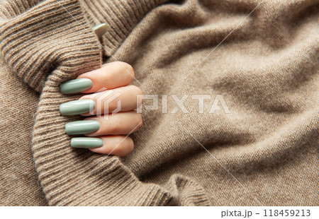 Elegant hand with long green nails holding a textured beige sweater during autumn fashion season Elegant hand with long green nails holding a textured beige sweater during autumn fashion season 118459213