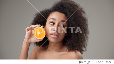 Beauty, vitamins and healthcare concept - beautiful African American woman with curly afro hairstyle and clean, healthy skin holding orange halves in her hands posing and looking at the camera 118460309