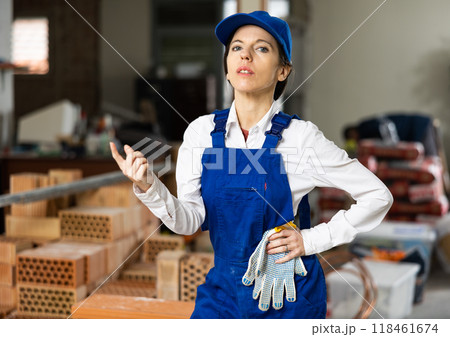 Female builder wearing overalls and cap posing at construction site, looking at camera 118461674