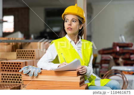 Woman foreman in a yellow vest and a protective helmet keeps track of bricks 118461675