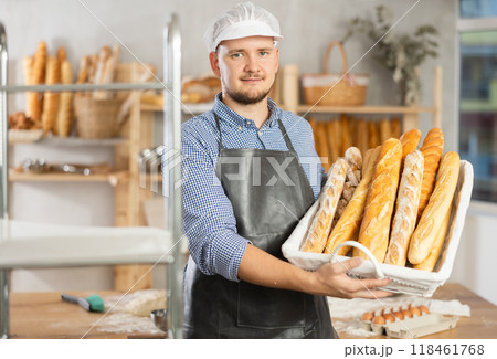 Male baker holds basket with finished products, shows many different baguettes Male baker holds basket with finished products, shows many different baguettes 118461768