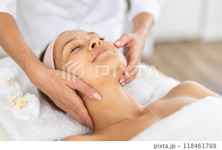 Young woman client gets procedure of rejuvenating massage face skin on cosmetologist visit Young woman client gets procedure of rejuvenating massage face skin on cosmetologist visit 118461788