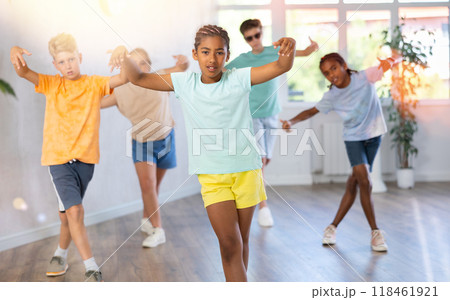 Positive juvenile girl engaged in Breakdancing in training room with children's group 118461921