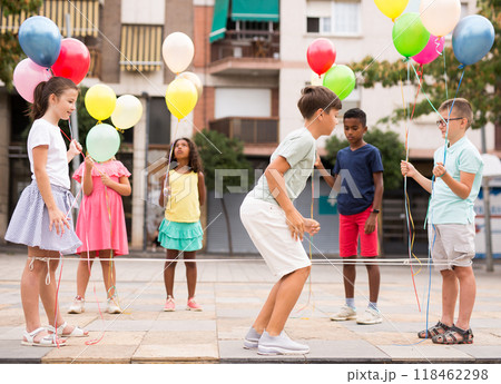 Happy tweenagers with balloons playing chinese jump rope in yard Happy tweenagers with balloons playing chinese jump rope in yard 118462298