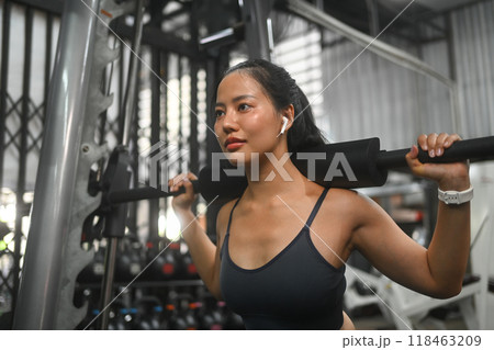 Focused sporty woman doing squat exercise with a barbell in a gym 118463209