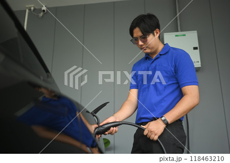 Handsome asian man plugging in an electric car. Renewable energy and transportation concept 118463210