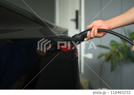 Man plugging in the charger into a socket of electric car. Green and sustainable transportation concept 118463252