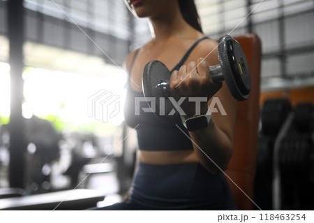 Close up of young athlete female wearing a fitness tracker on her wrist working out with dumbbells in a gym Close up of young athlete female wearing a fitness tracker on her wrist working out with dumbbells in a gym 118463254