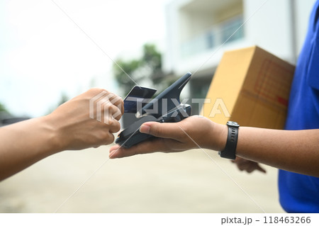 Unrecognizable man making contactless payment with a credit card while receiving parcel box from delivery man Unrecognizable man making contactless payment with a credit card while receiving parcel box from delivery man 118463266