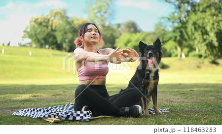 Active young woman sitting next to her border collie dog and stretching her arms after workout 118463283