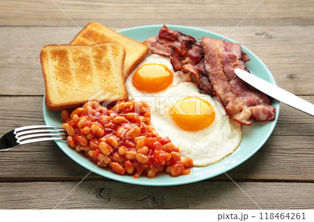 Traditional full English breakfast - fried eggs, beans, bacon and toast on grey background. Traditional full English breakfast - fried eggs, beans, bacon and toast on grey background. 118464261