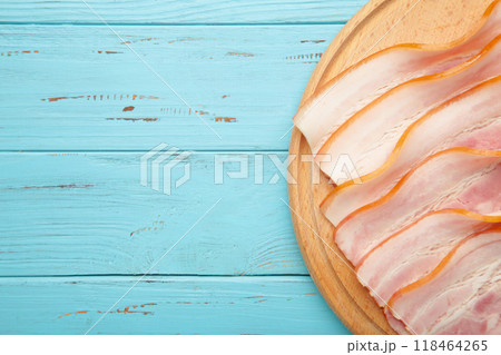 Fresh raw sliced bacon on the wooden cutting board on blue. 118464265