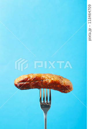 Grilled sausage on a fork on blue background with copy space Grilled sausage on a fork on blue background with copy space 118464709