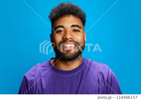 Portrait of young African-American man smiling widely against blue background, and looking at camera. Positive people. 118466157