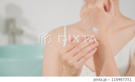 The advertising template photo for skincare product, a female with white dress is showing white cream texture on the back of hand. Front view on blurred bathroom background, copy space for adding text 118467351