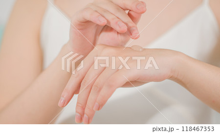 Frontal close-up photo of a woman wearing a white strapless dress preparing to apply a drop of lotion to the back of her hand. Advertising template, blank space for adding design elements 118467353