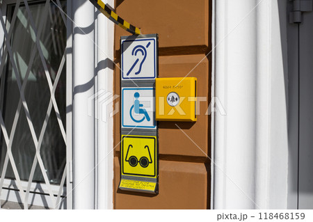 Sign with international sign of person with disabilities in wheelchair on wall near entrance to building. Deaf and blind person symbol with braille text 118468159
