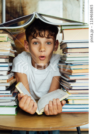 A cheerful boy looks through two stacks of books. On the head is a book in the shape of a roof A cheerful boy looks through two stacks of books. On the head is a book in the shape of a roof 118468665