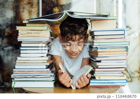 A cheerful boy looks through two stacks of books. On the head is a book in the shape of a roof 118468670