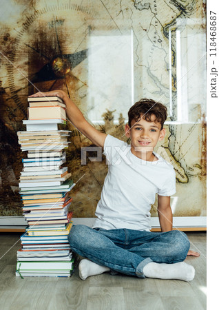 A boy sits next to a stack of books and holds them with his hand A boy sits next to a stack of books and holds them with his hand 118468687