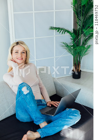 Beautiful blonde woman working on laptop online on sofa at home Beautiful blonde woman working on laptop online on sofa at home 118469752