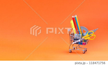 Shopping cart with school supplies on orange background. Preparing for school, buying stationery concept. Banner minimal copy space Shopping cart with school supplies on orange background. Preparing for school, buying stationery concept. Banner minimal copy space 118471756