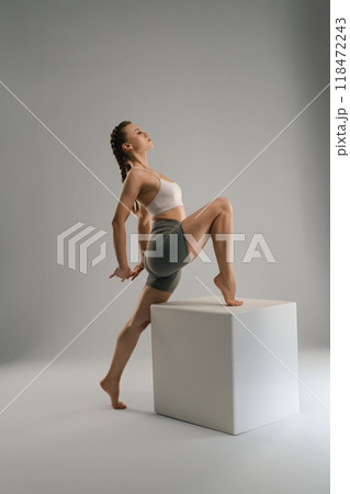 Female dancer performing a modern pose on a white cube in a studio Female dancer performing a modern pose on a white cube in a studio 118472243