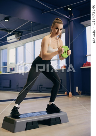 Woman performing a step workout using dumbbells in a gym studio 118472246