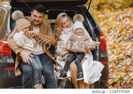 Happy family resting after day spending outdoor in autumn park. Father, mother and two children sitting inside car trunk, smiling. Family holiday and traveling concept. Happy family resting after day spending outdoor in autumn park. Father, mother and two children sitting inside car trunk, smiling. Family holiday and traveling concept. 118474380