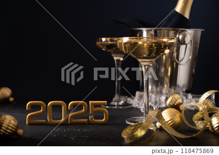 New Year 2025. Champagne in wine glasses, Christmas gold baubles and festive decorations on black background. Close up. Holiday greeting card with copy space. Happy New Year. New Year 2025. Champagne in wine glasses, Christmas gold baubles and festive decorations on black background. Close up. Holiday greeting card with copy space. Happy New Year. 118475869