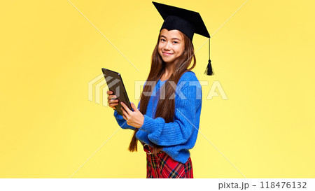 Modern student. Generation Z. Charming young lady, student with tablet looking at camera dressed stylish outfit and graduation cap. 118476132