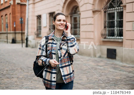 Beautiful stylish woman in trendy wear spending time on street using smartphone. Happy girl with backpack talking on the mobile phone. Urban lifestyle concept Beautiful stylish woman in trendy wear spending time on street using smartphone. Happy girl with backpack talking on the mobile phone. Urban lifestyle concept 118476349