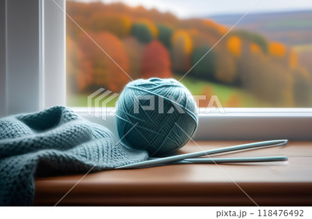 Unfinished knitting by window in fall. Blue ball of wool and needles. Autumn sadness, melancholy. Cozy evening at home 118476492