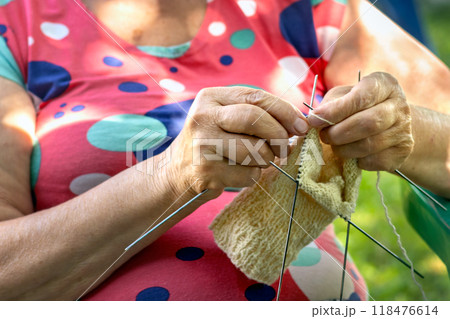 Hands of an elderly woman knitting socks for grandchildren. Pensioner enjoying her hobby in yard on sunny summer day. Close-up 118476614