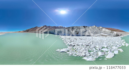 The Kyzyl-Asker glacier in Kyrgyzstan offers a stunning 360-degree panorama, with a turquoise lake at the foot and a bright blue sky above it. The snow-capped peaks of the mountains rise majestically. 118477033