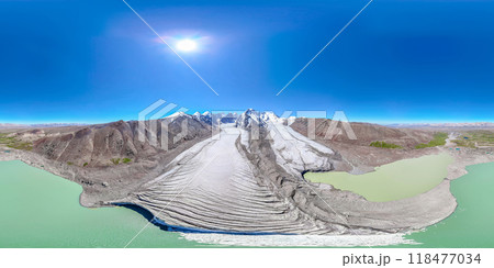 The Kyzyl-Asker glacier in Kyrgyzstan offers a stunning 360-degree panorama, with a turquoise lake at the foot and a bright blue sky above it. The snow-capped peaks of the mountains rise majestically 118477034