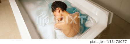 A woman leisurely bathes in a foamy bathtub, barechested and relaxed 118478077